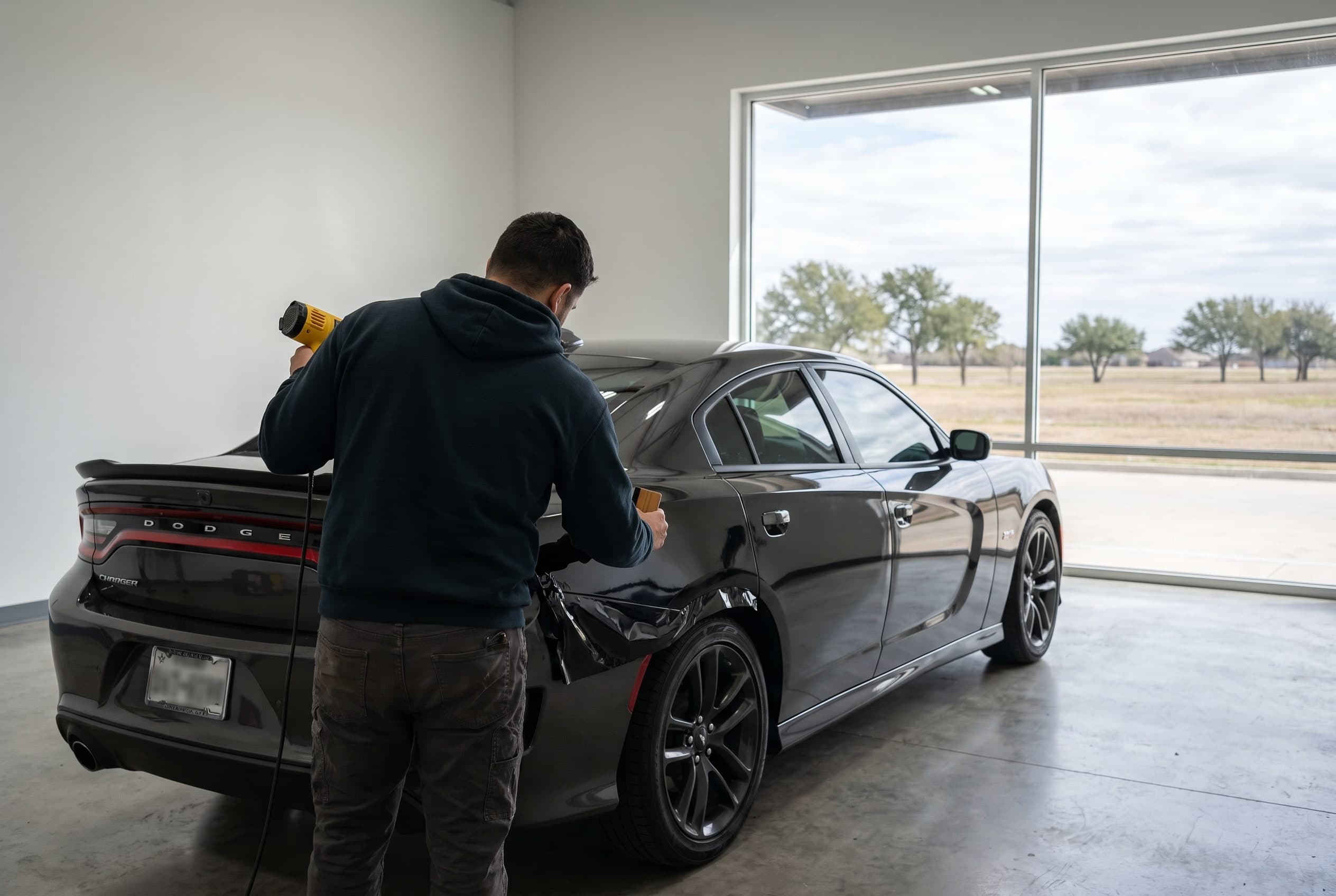 Installer heat-gunning gloss black cast vinyl onto the door of a Dodge Charger in a Dallas wrap bay