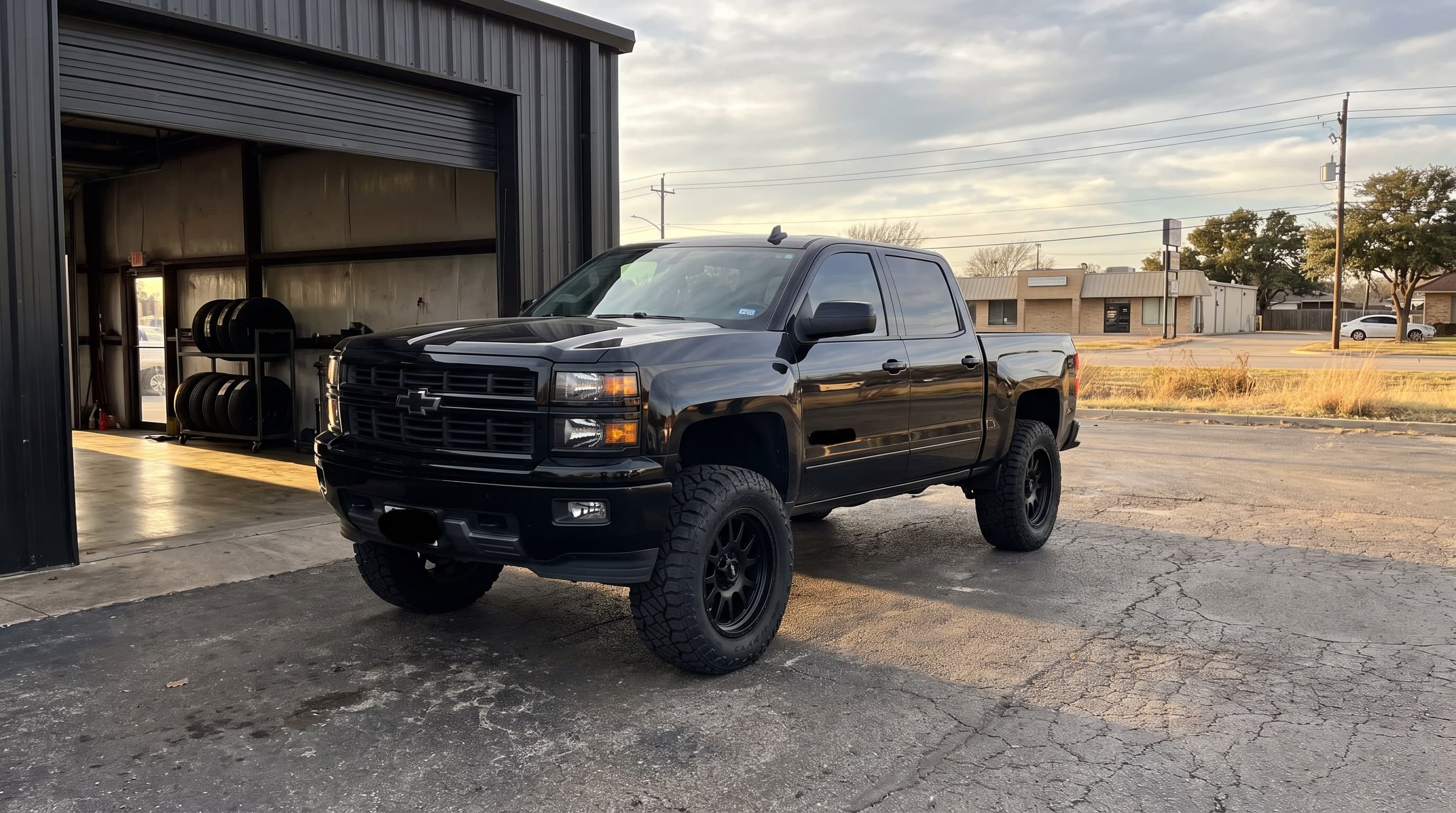 Lifted black Chevrolet Silverado on 35-inch tires parked outside the Metroplex Customs shop bay on South Belt Line Road in Irving, Texas