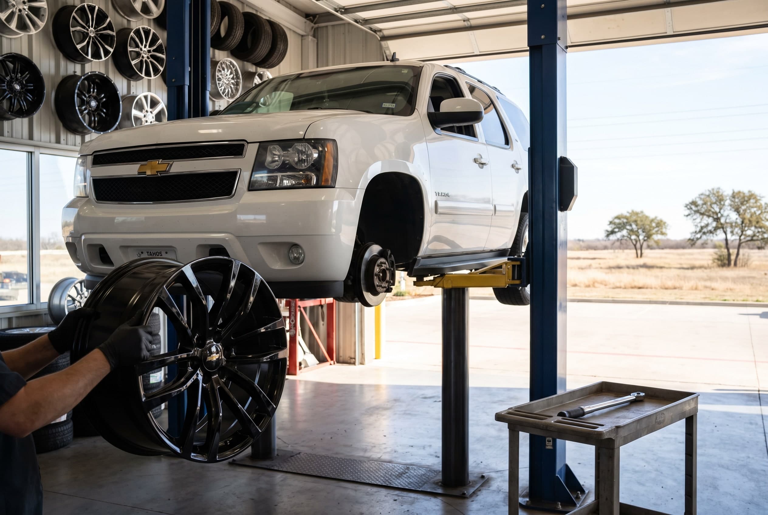 Gloss black 22-inch wheels being fitted to a white Chevrolet Tahoe on a lift in an Irving, TX wheel shop